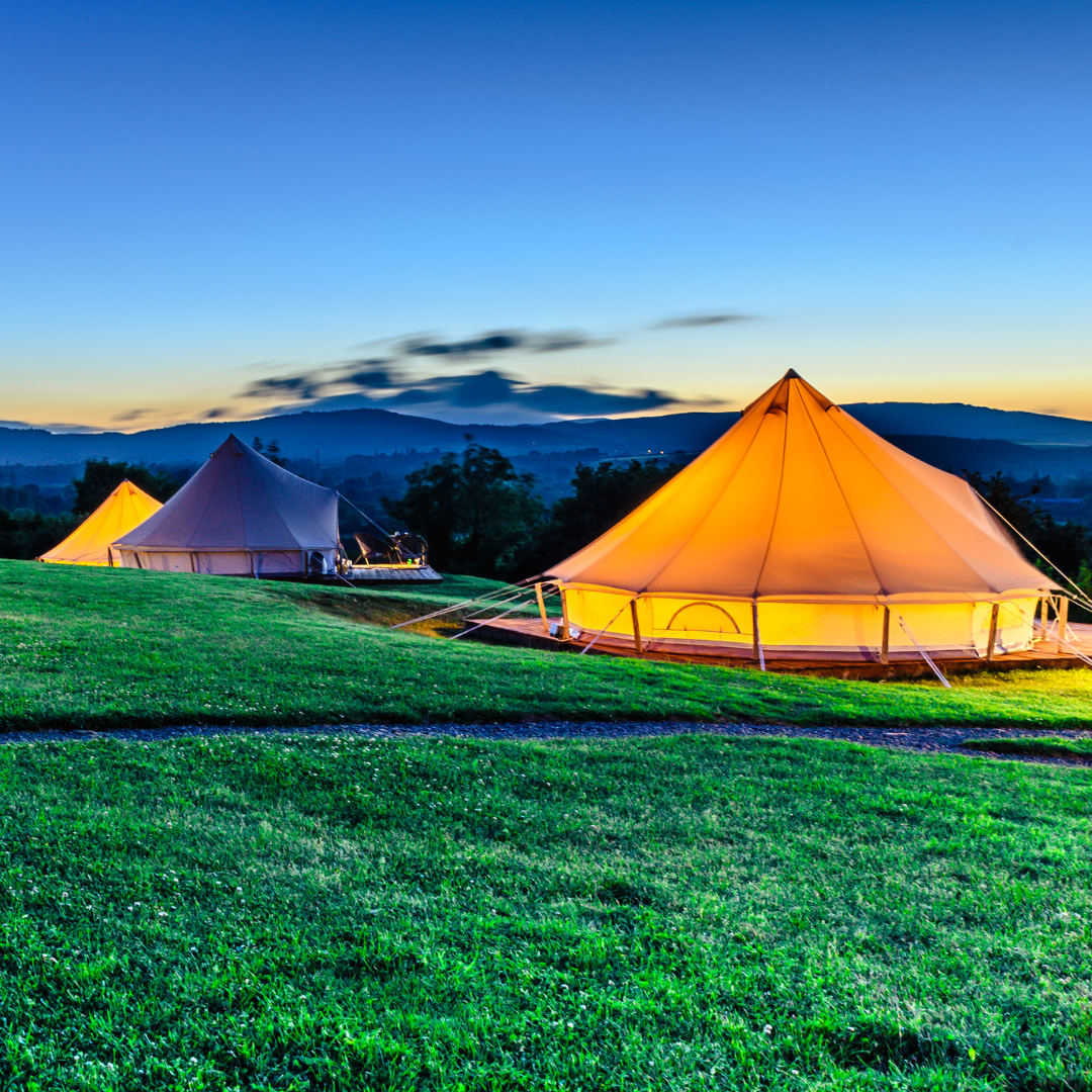 Bell tents at sundown, set up on wood platforms, glowing from interior lighting.