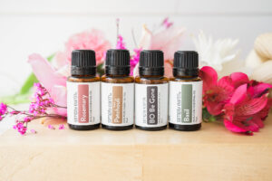 Four essential oils placed side by side displayed in front of flowers